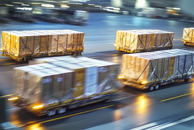 Cargo wrapped in clear plastic being transported on carts inside a brightly lit logistics warehouse, representing efficient shipping operations.